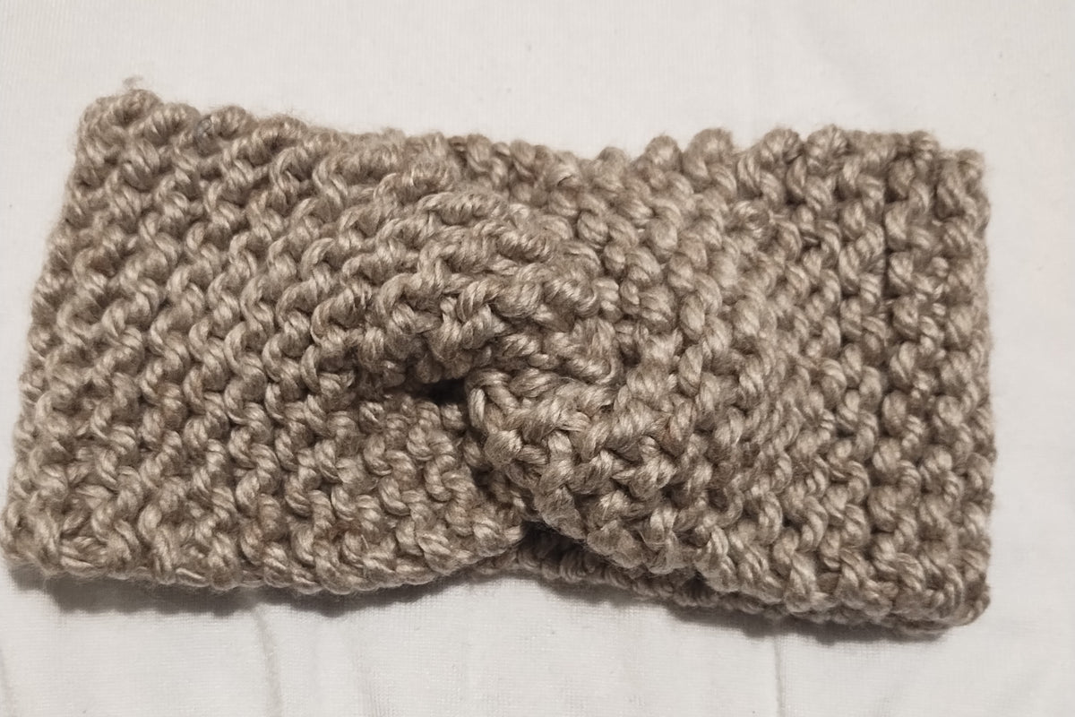 A chunky knit twist-front ear warmer headband in a gray color, laid flat on a white fabric background.